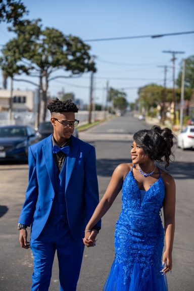 Prom Sendoff Two individuals in formal blue attire walking hand-in-hand along a street.
